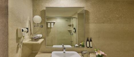 A bathroom with a large mirror, a sink, a hairdryer, and a shower.