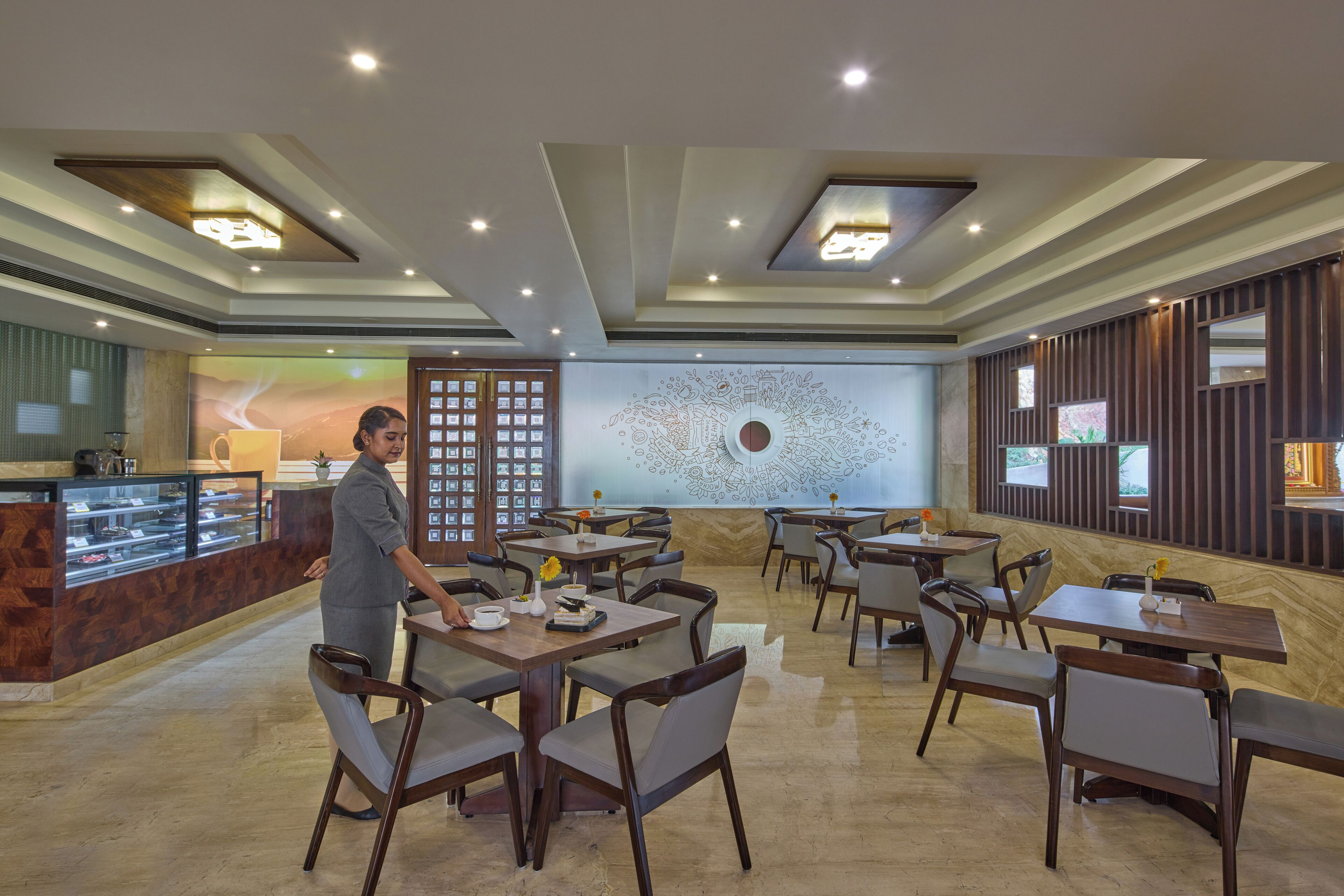A restaurant with multiple tables and chairs, a counter with a display case, and a wall with a mural.