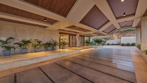 A spacious indoor area with a modern design, featuring a long corridor with a tiled floor, potted plants, and a wooden ceiling structure. - Regenta Hubbali (Hubli)