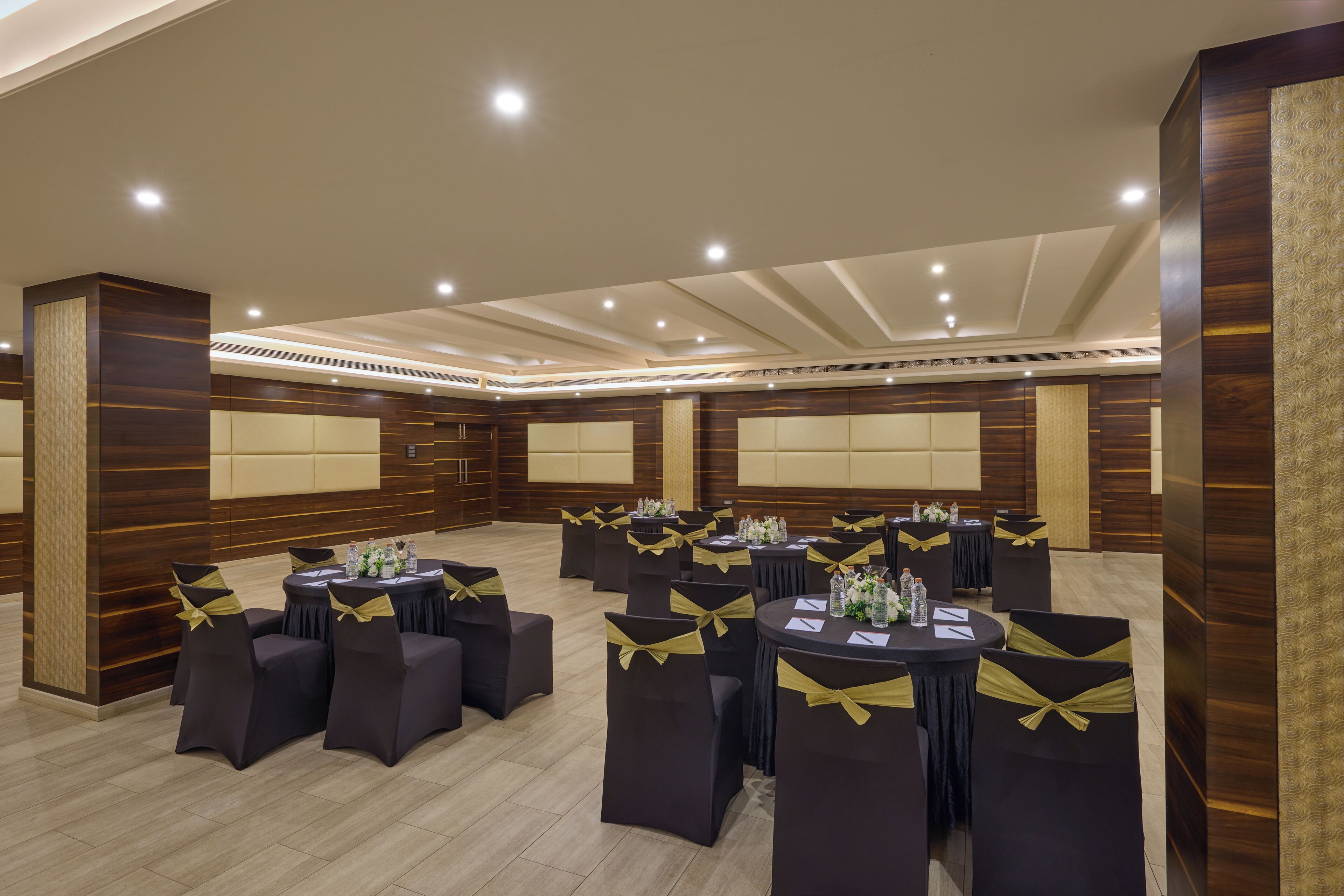 A conference room with multiple tables, chairs, and a high ceiling with recessed lighting.