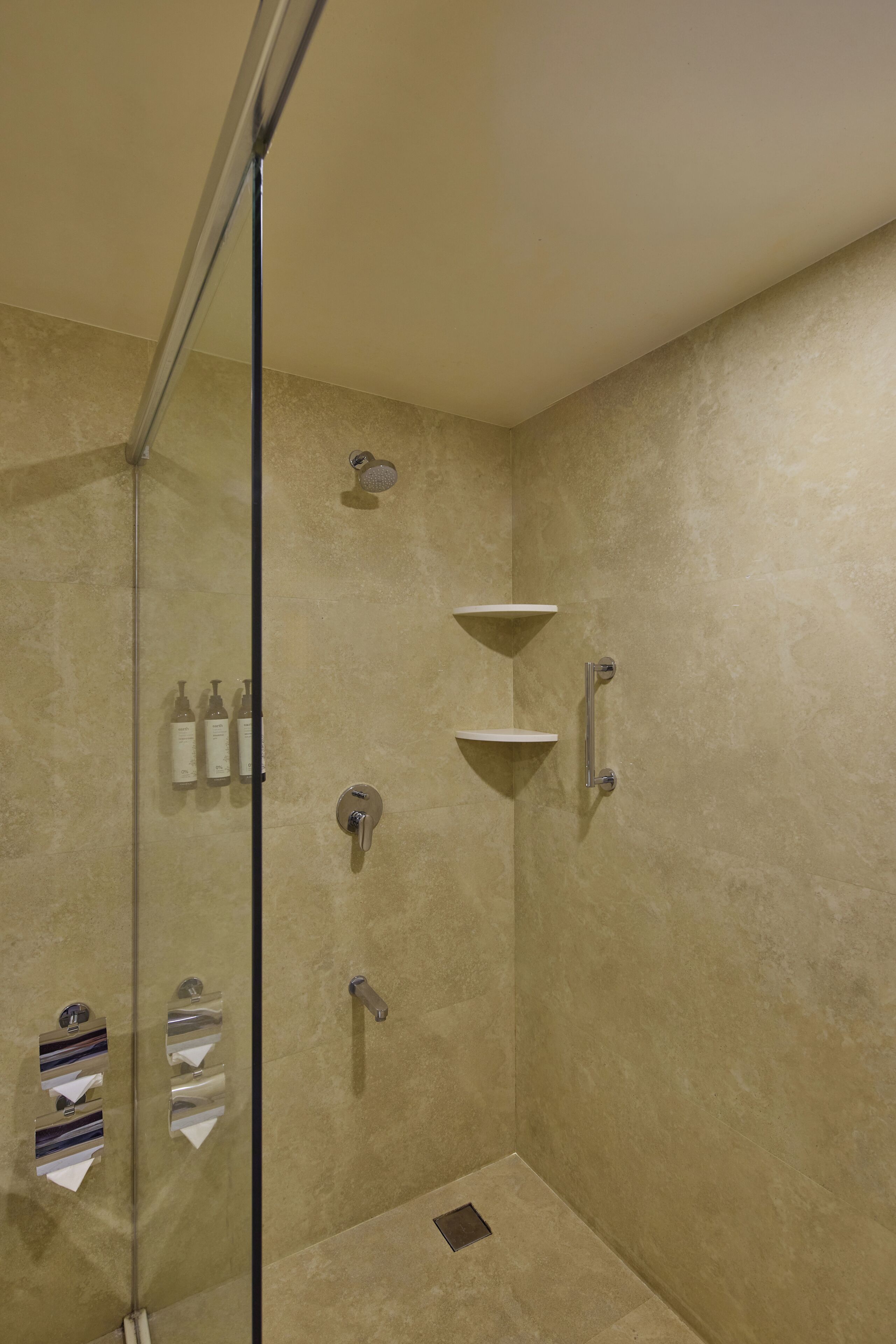 Un espace douche doté d’une porte en verre, d’un pommeau de douche à main, d’un robinet mural et d’une étagère pour les articles de toilette.