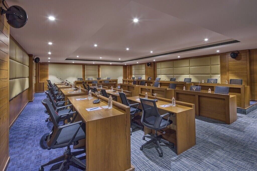A conference room with multiple tables and chairs, equipped with microphones and water bottles.