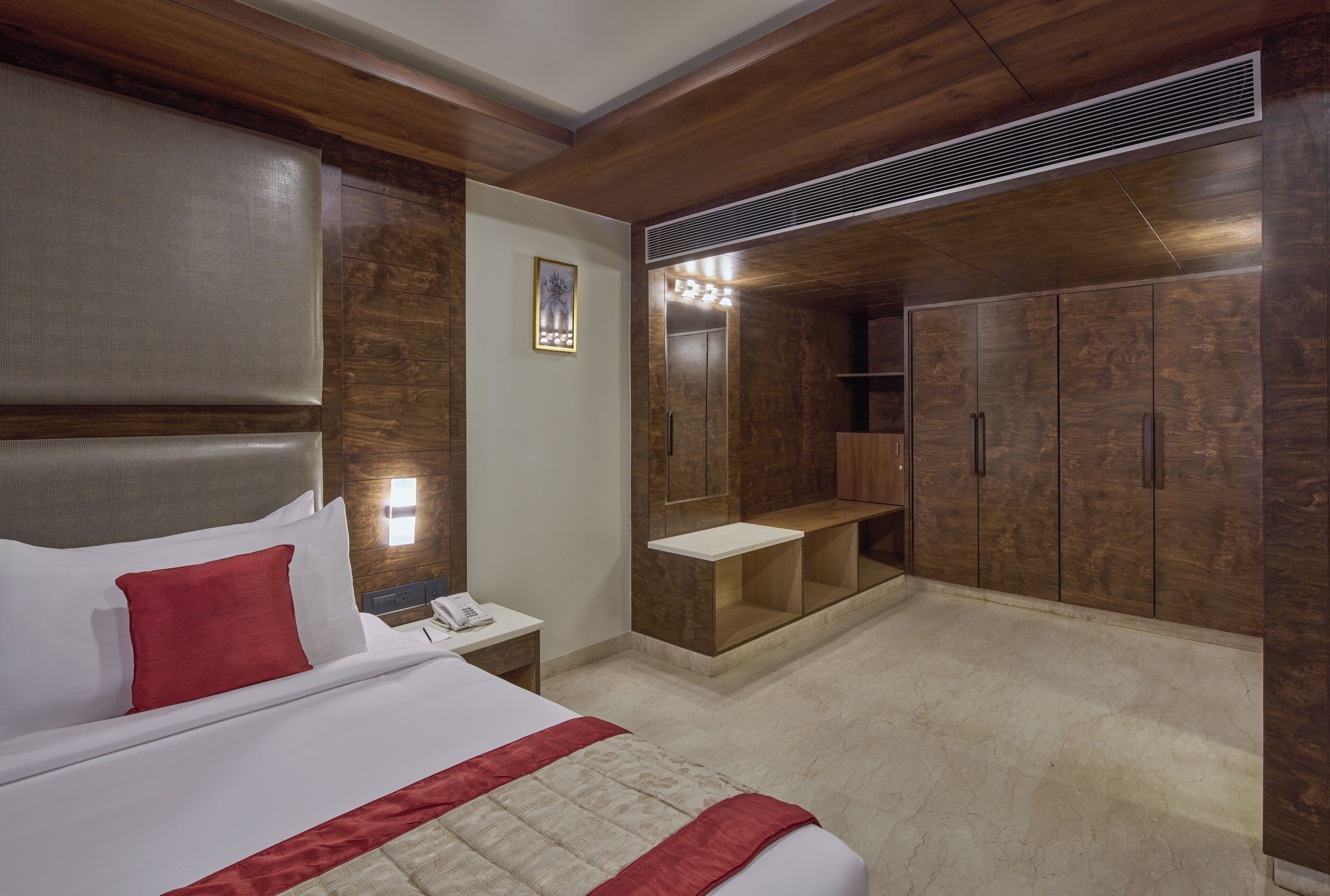 Une chambre d’hôtel avec un grand lit, une table de chevet, un miroir, une armoire et un petit coin salon.