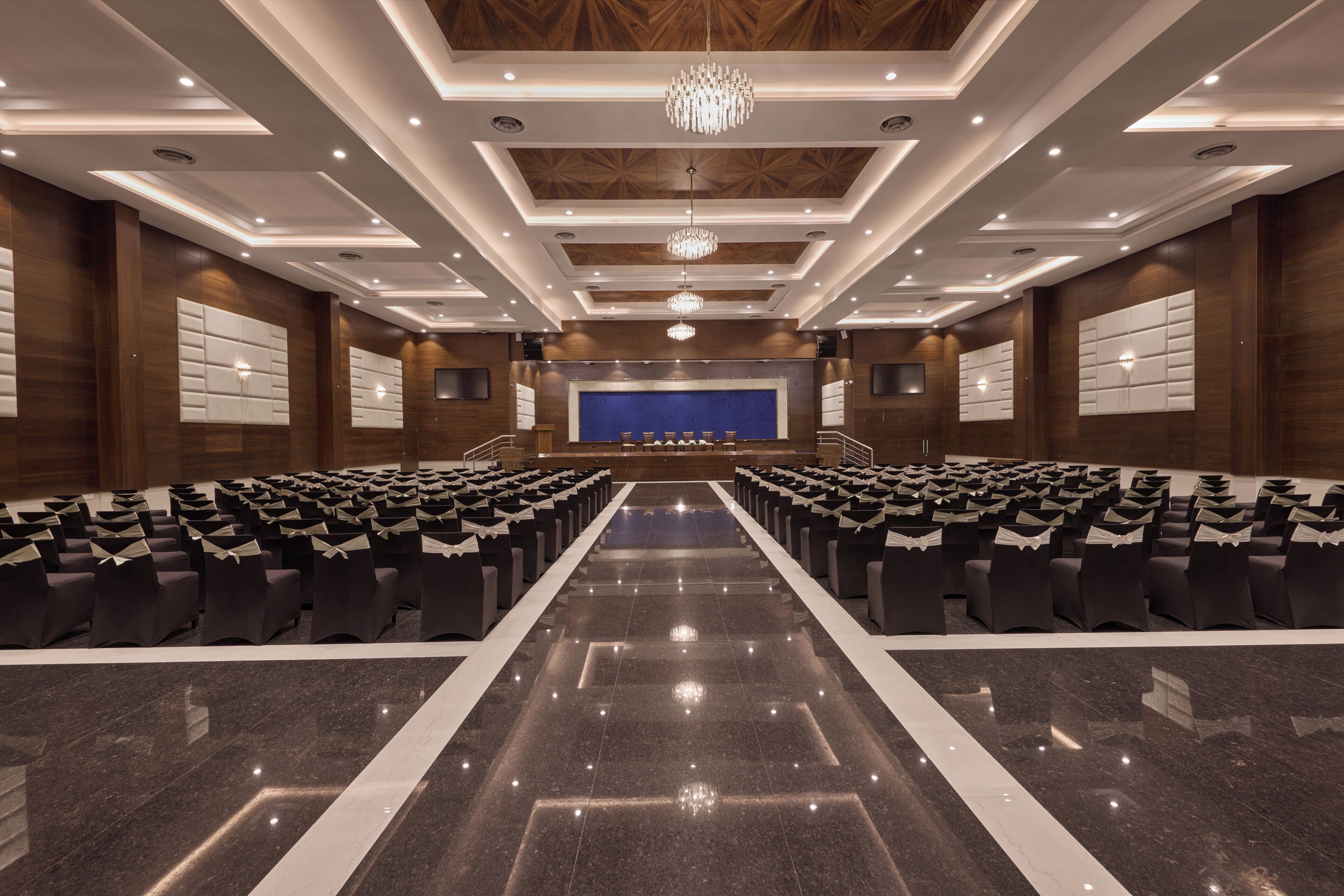 A conference room with rows of chairs, a stage, and a chandelier.