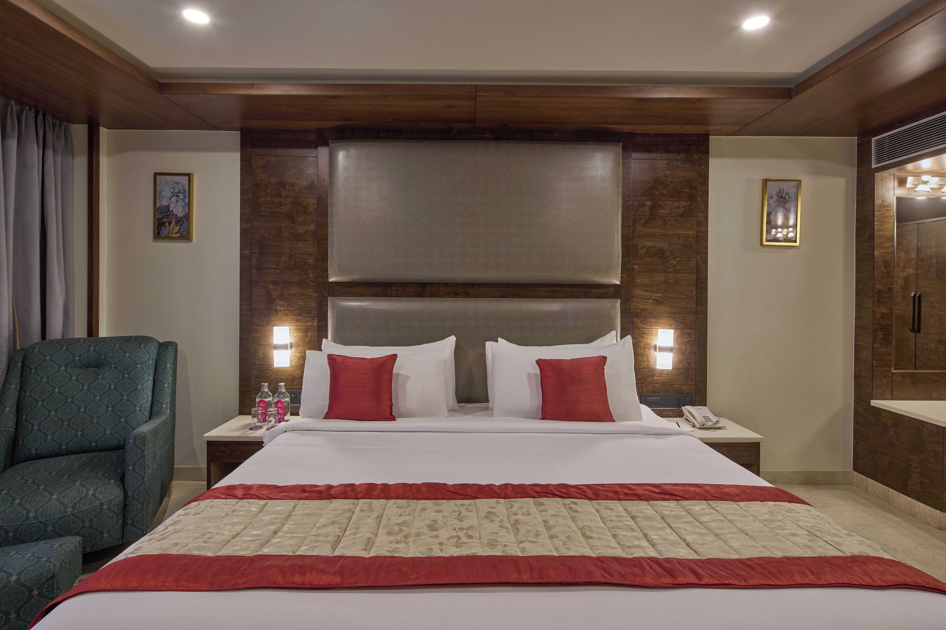 A hotel room with a large bed, two bedside tables, a chair, and a wooden headboard.