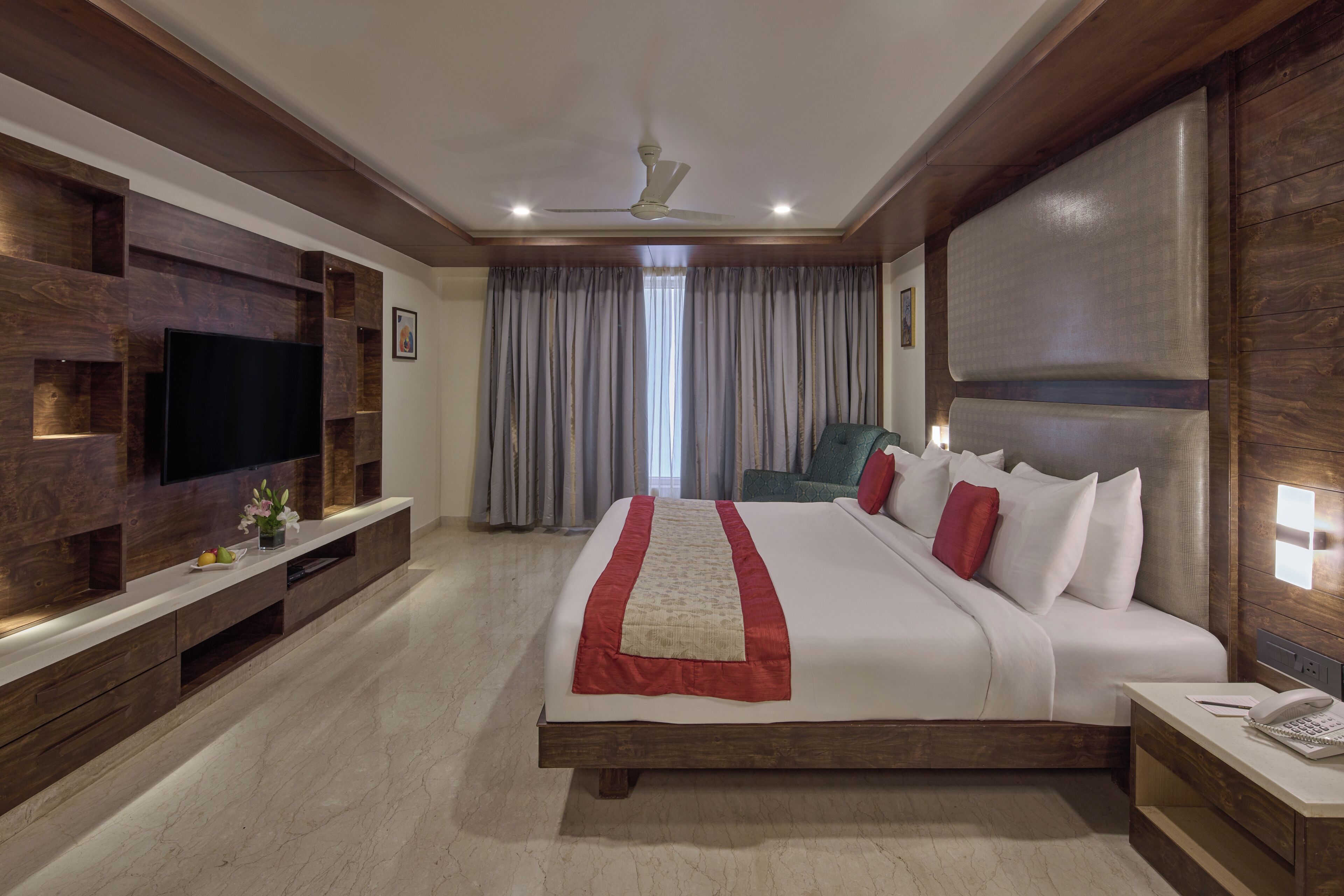 A hotel room with a large bed, a TV mounted on the wall, a desk with a phone, and a ceiling fan.