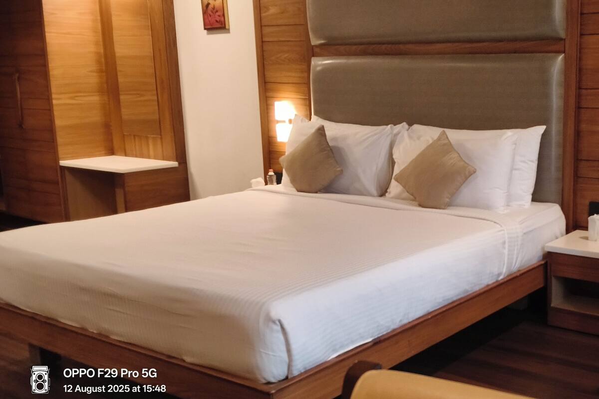 A hotel room with a large bed, a green upholstered armchair, and a nightstand with a bottle and tissue.