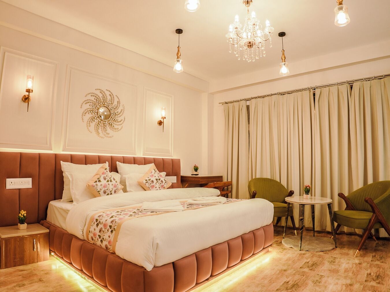 A well-lit bedroom with a large bed, a chandelier, a green armchair, and a small round table.
