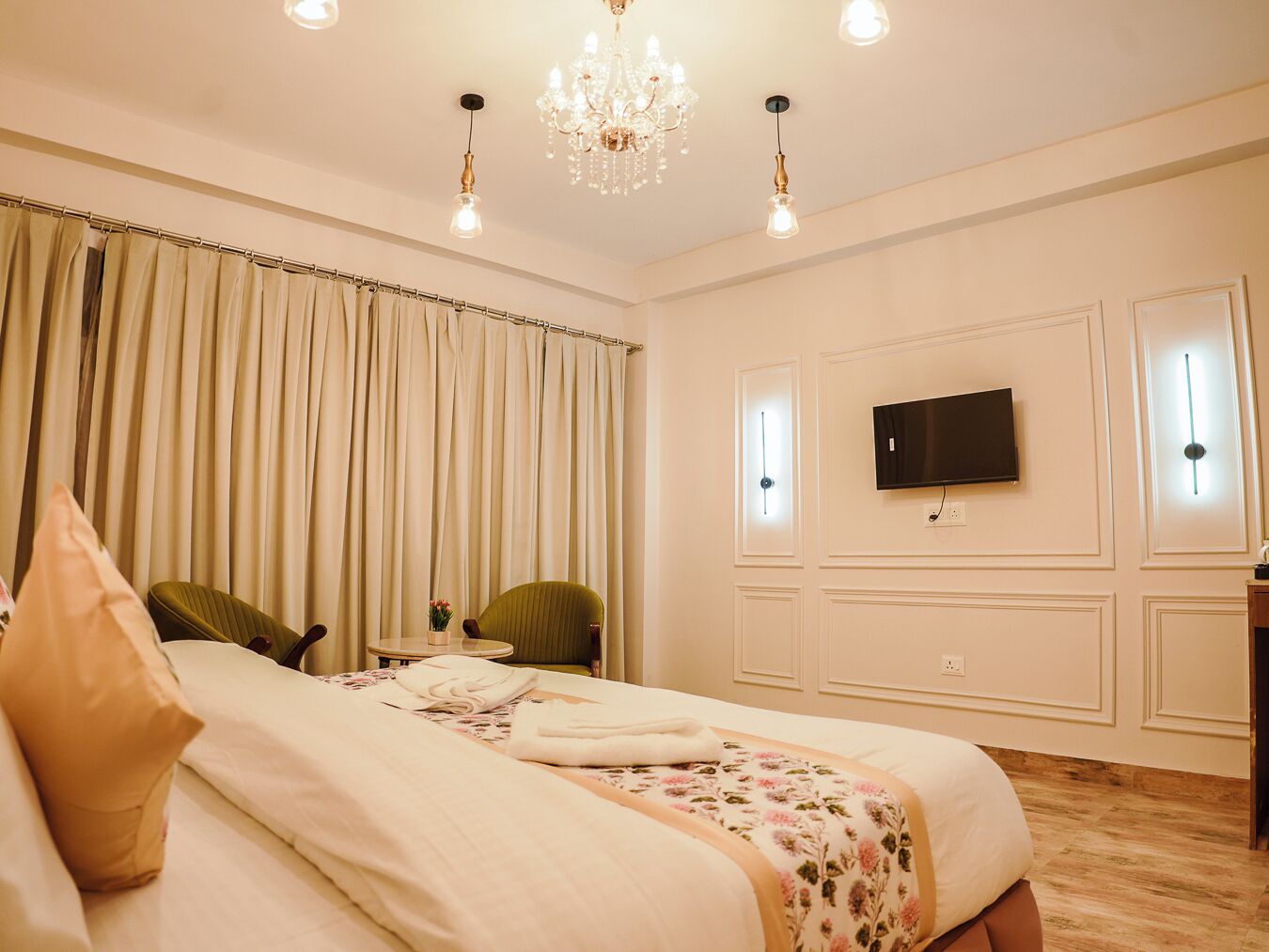 A hotel room with a large bed, a television mounted on the wall, and a chandelier.