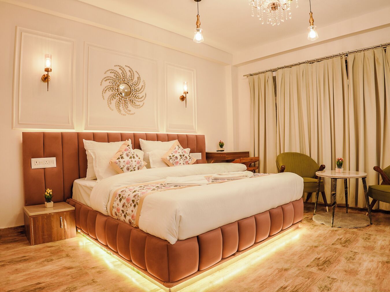 A spacious bedroom with a large bed, a wooden nightstand, a small table, and a green armchair.