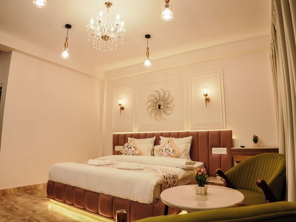A modern bedroom with a large bed, a round table, a green armchair, and decorative wall sconces.
