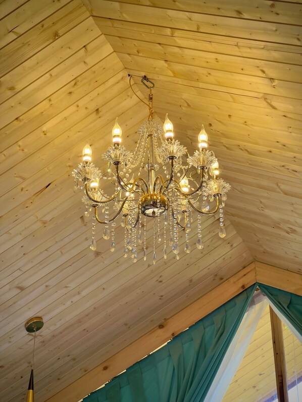 A chandelier with multiple arms and crystal decorations in a tent-like room with wooden walls.