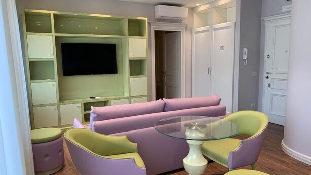 Een moderne woonkamer met een bank, twee fauteuils, een glazen salontafel en een aan de muur bevestigde televisie.