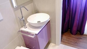 Een badkamer met een wit wastafelmeubel, een spiegel en een paarse kast.