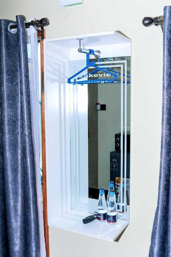 A bathroom with a mirror, a towel rack, and a shelf with bottled water. - Lux Suites Lakeview Cottages Ruiru (Ruiru)