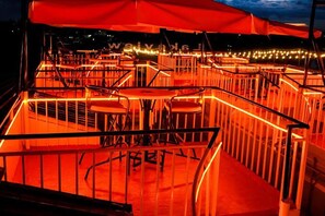 An outdoor seating area with tables and chairs, surrounded by a railing and illuminated by warm lighting. - Lux Suites Lakeview Cottages Ruiru (Ruiru)