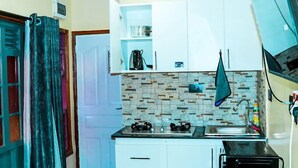 A compact kitchen with white cabinets, a tiled backsplash, a gas stove, a sink, and a microwave. - Lux Suites Lakeview Cottages Ruiru (Ruiru)