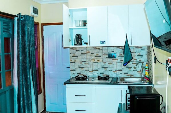 A compact kitchen with white cabinets, a tiled backsplash, a gas stove, a sink, and a microwave. - Lux Suites Lakeview Cottages Ruiru (Ruiru)