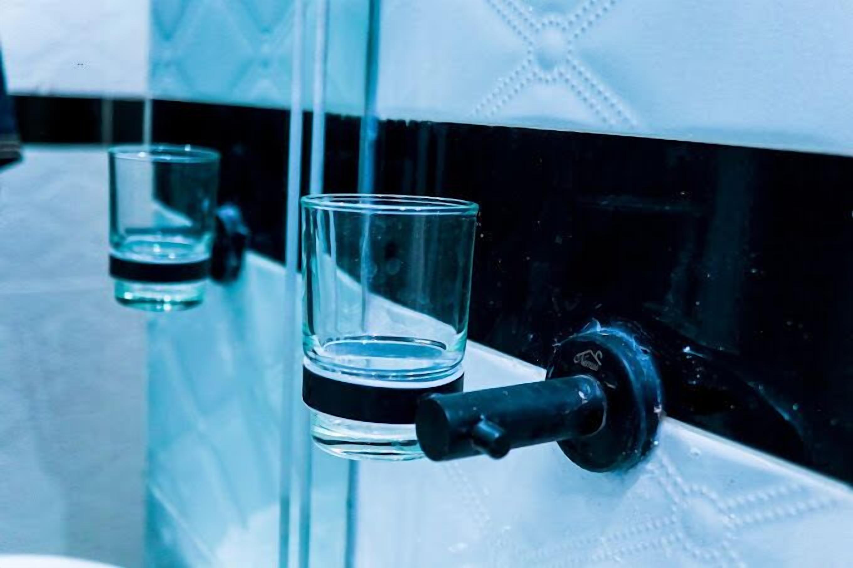 A glass of water on a reflective surface with a faucet.