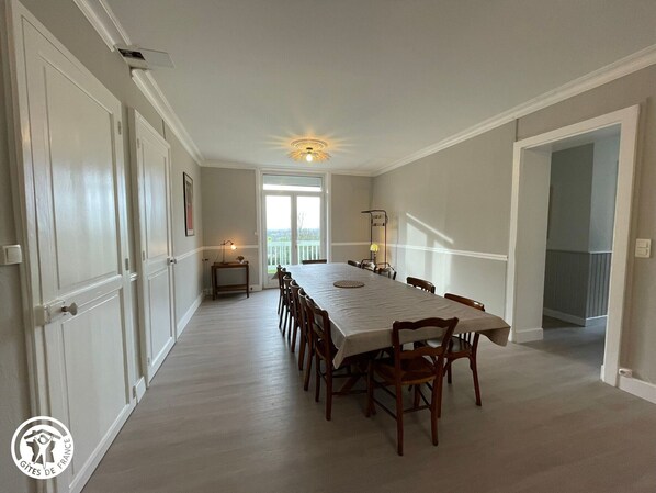 A dining room with a long table and chairs, a ceiling fan, and a view through a glass door to the outside.