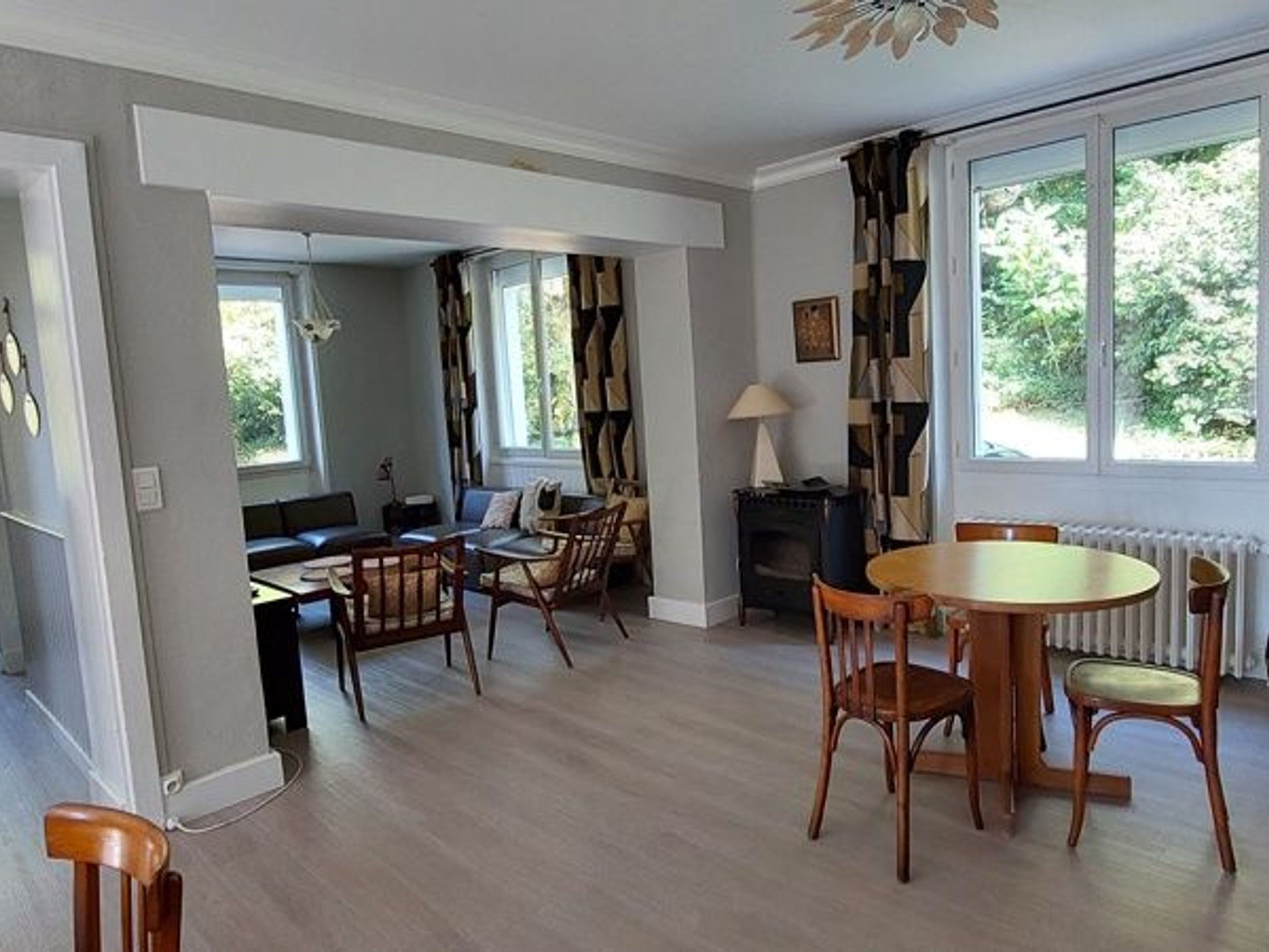 Een kamer met een eettafel, stoelen, een bank, een open haard en grote ramen.