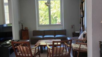 Een woonkamer met een bank, twee stoelen, een televisie en een raam met uitzicht op groen.
