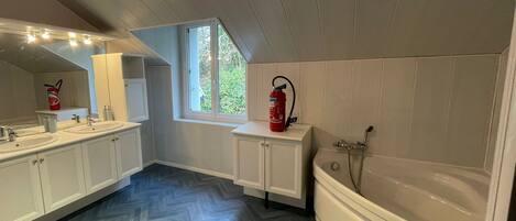 Een badkamer met een groot raam, een bad en een wastafel met twee kommen.