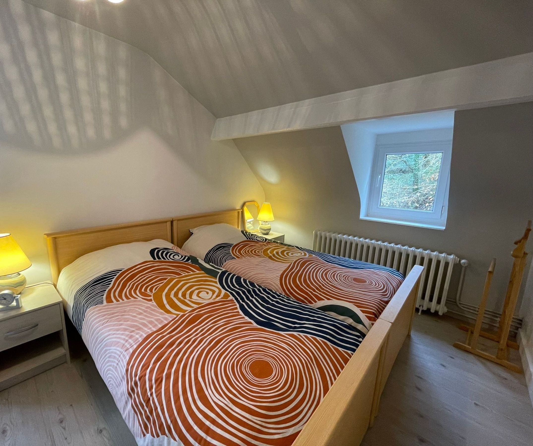 Un dormitorio con cama, dos lámparas de noche, una ventana y un radiador.