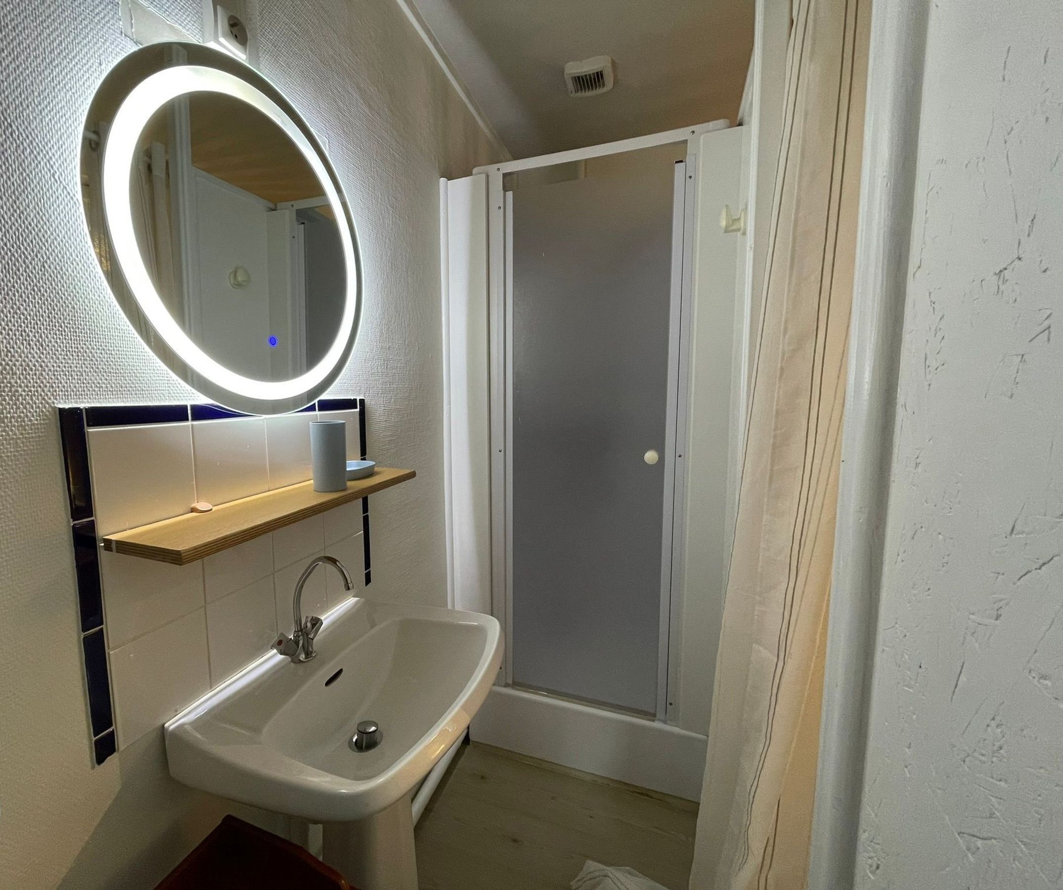 A bathroom with a white sink, a mirror with a light, a shower, and a towel rack.