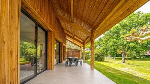 Een overdekt terras met een houten plafond en uitzicht op een weelderige tuin.