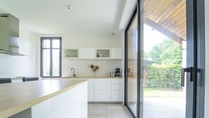 Een moderne keuken met een houten aanrecht, witte kasten, een ingebouwde oven en een grote schuifpui naar een tuin.