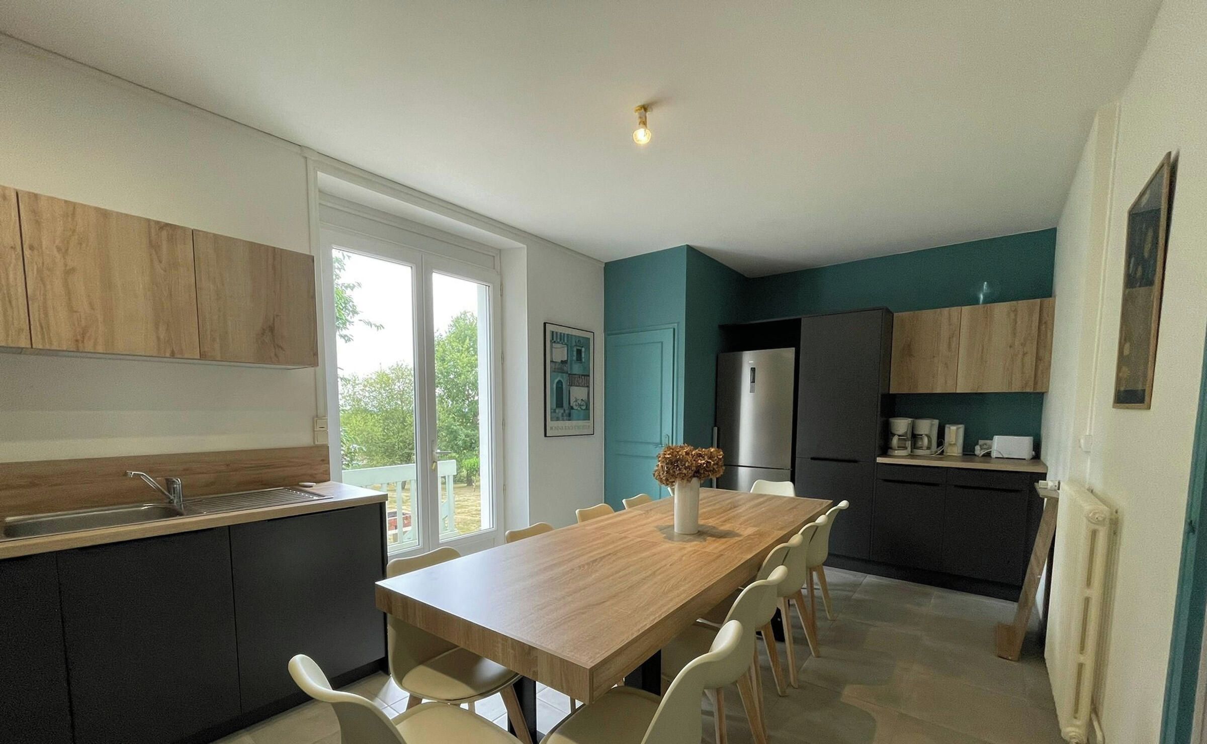 A modern kitchen with a dining table and chairs, a refrigerator, and a window providing a view of the outdoors.