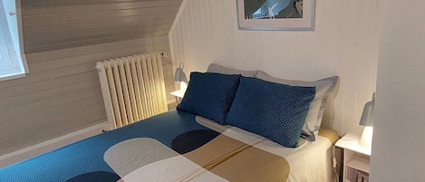 A bedroom with a bed, a radiator, a wall-mounted picture, and a window.