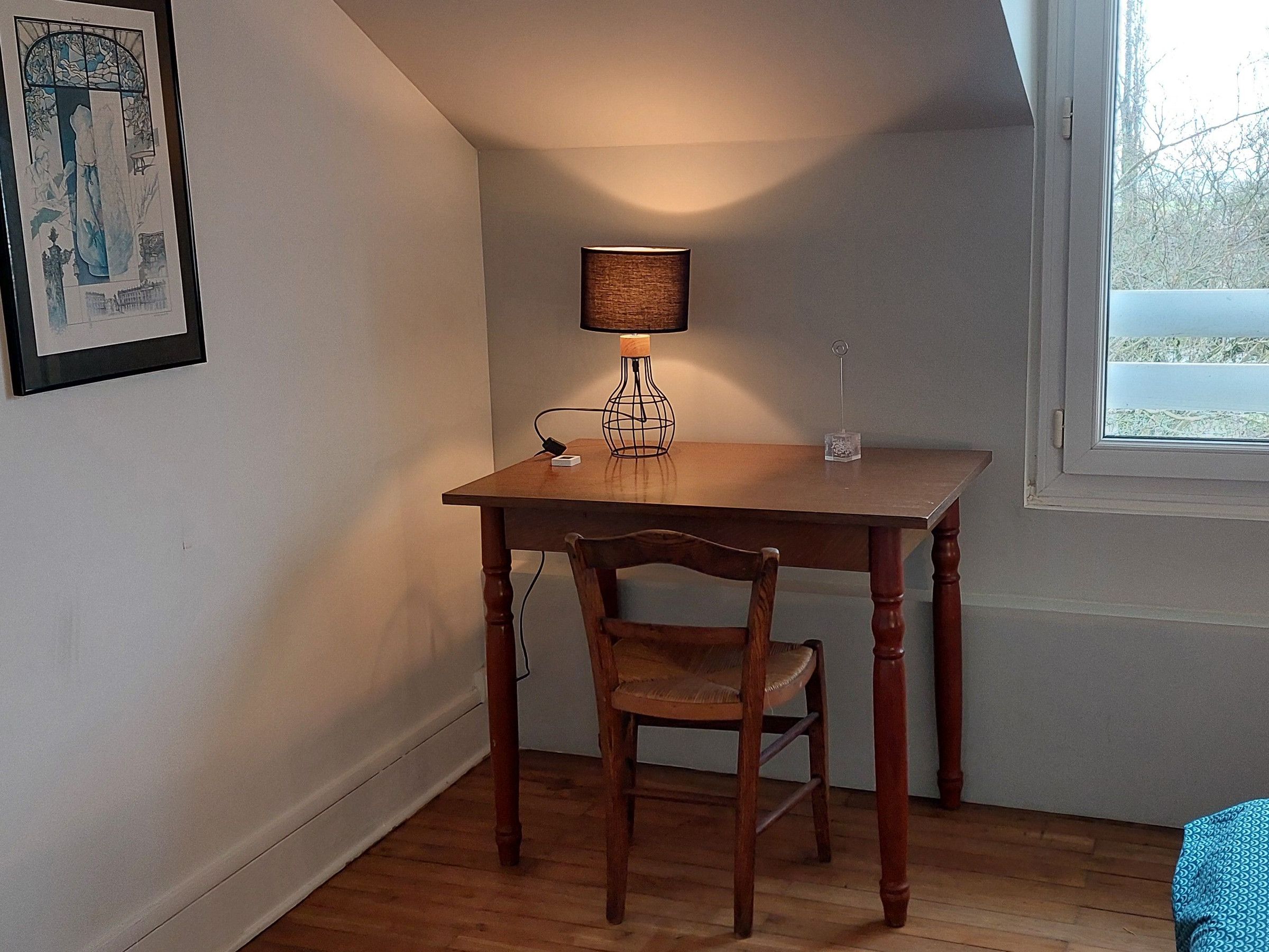 A small room with a wooden desk, a chair, a lamp, and a framed picture on the wall.