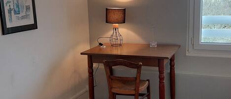 A small room with a wooden desk, a chair, a lamp, and a framed picture on the wall.