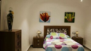 Un dormitori amb un llit, dues taules de nit, un prestatge de fusta i dos quadres penjats a la paret.