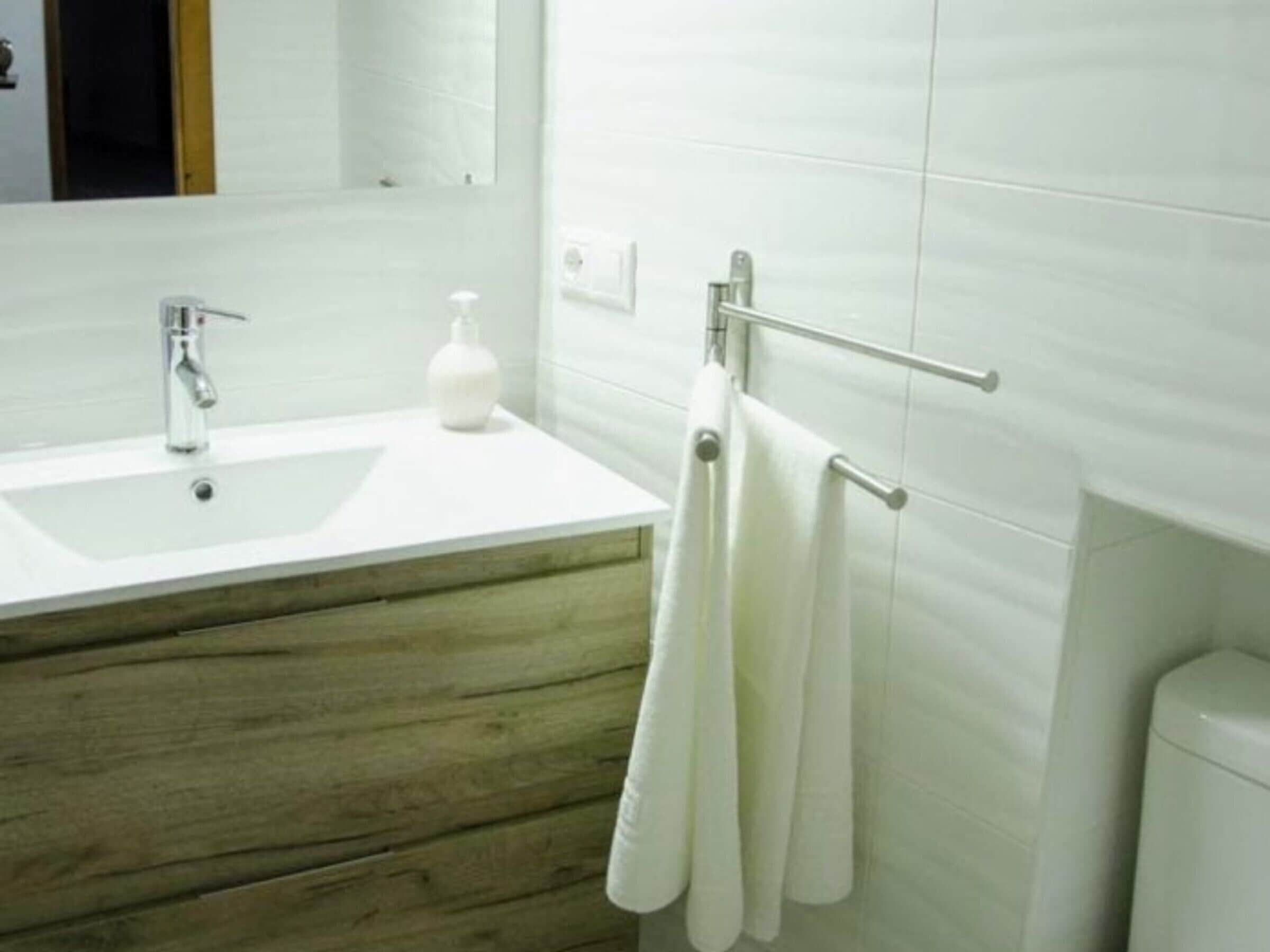 Un bagno con un lavandino bianco, un mobile contenitore in legno e un porta asciugamani con asciugamani.