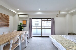 Habitación de hotel con una mesa de comedor de madera, sillas, una cama y un ventanal con cortinas.