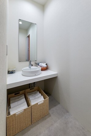 Un baño con un lavamanos blanco, un espejo y dos cestas de mimbre debajo del lavamanos.