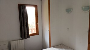 A small, single-bed room with a window, a radiator, and a wooden door. - Spacious apartment in Super Besse with pool and parking (Besse-et-Saint-Anastaise-Super Besse)