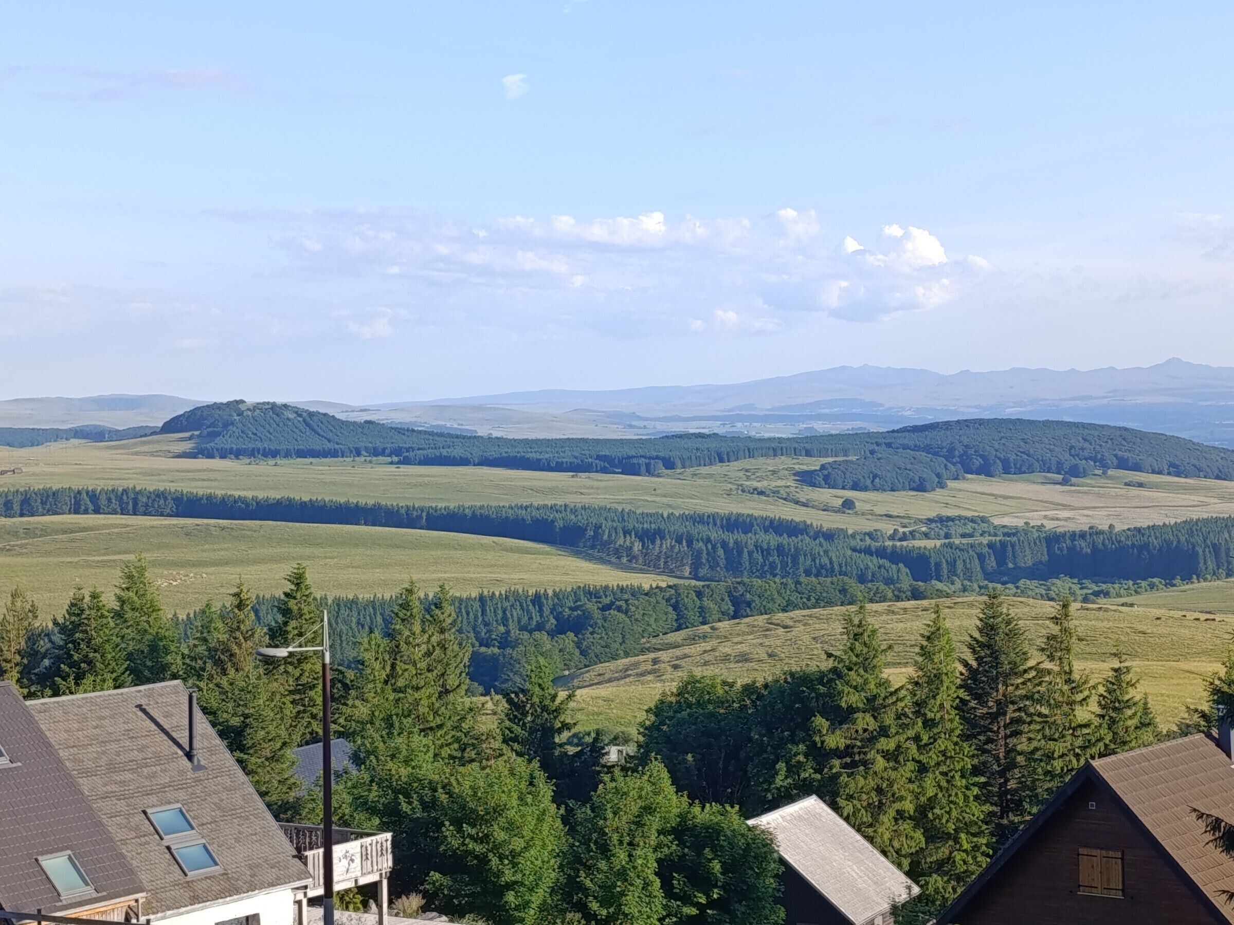 A panoramic view of a rural landscape with rolling hills, dense forests, and a clear sky.