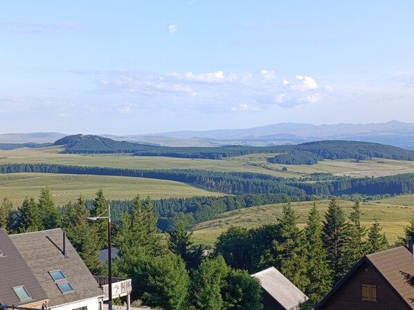 A panoramic view of a rural landscape with rolling hills, dense forests, and a clear sky.