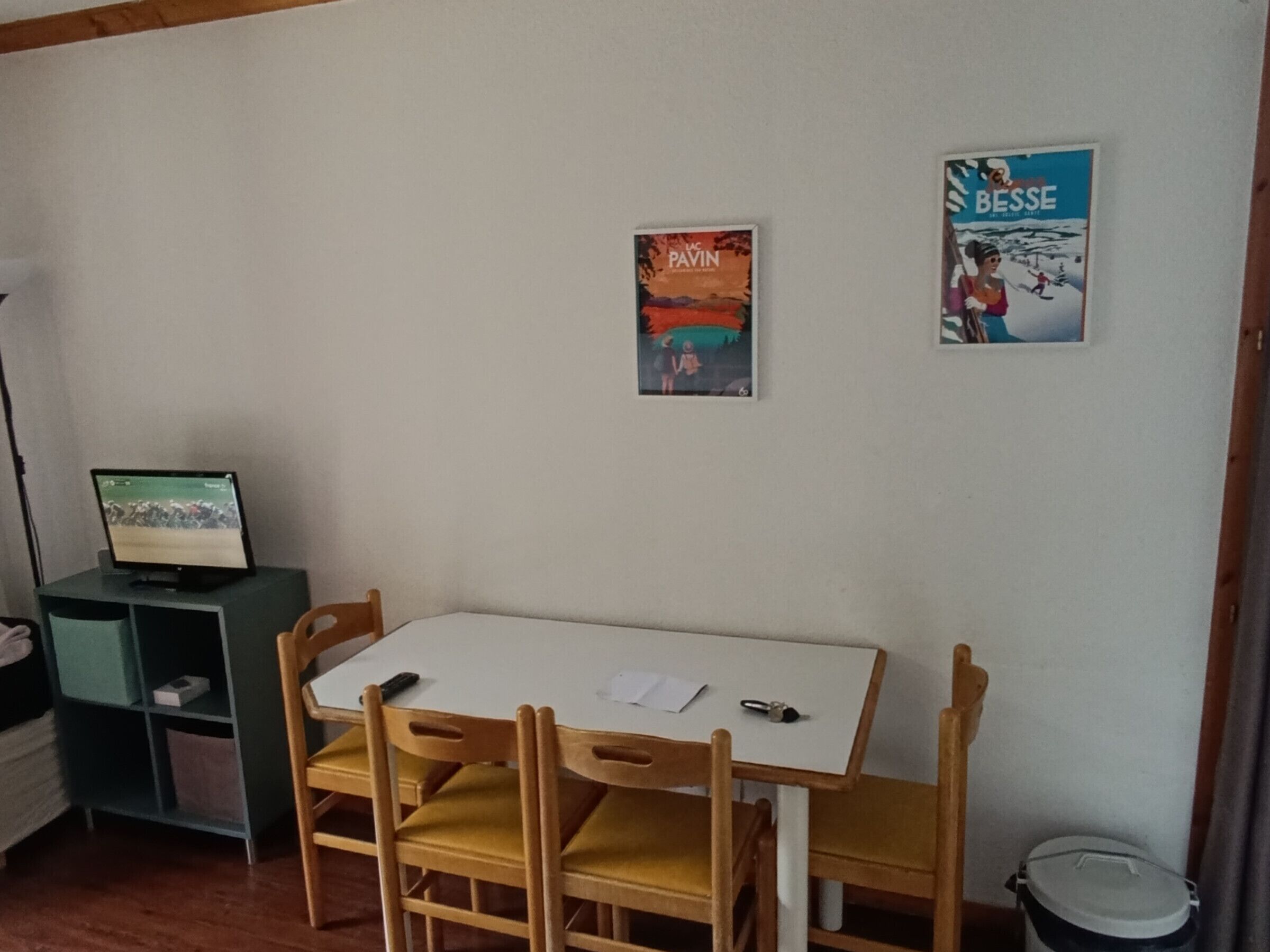 Ein Zimmer mit einem weißen Tisch, Holzstühlen, einem Computer auf einem Regal und zwei Bildern an der Wand.