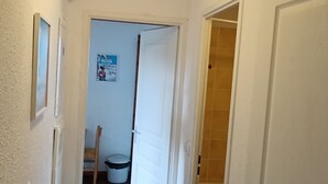 A narrow hallway with white walls, a door leading to a bathroom with a tiled shower, and a poster on the wall. - Spacious apartment in Super Besse with pool and parking (Besse-et-Saint-Anastaise-Super Besse)