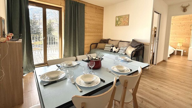 A dining area with a table set for four, a sofa, and a wooden floor. - Cozy apartment in Praz-sur-Arly with parking and balcony, near slopes, for 6 people (Praz-sur-Arly)