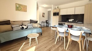 A modern living room with a sofa, a dining table with chairs, a kitchen area with cabinets and appliances, and a small side table. - Cozy apartment in Praz-sur-Arly with parking and balcony, near slopes, for 6 people (Praz-sur-Arly)