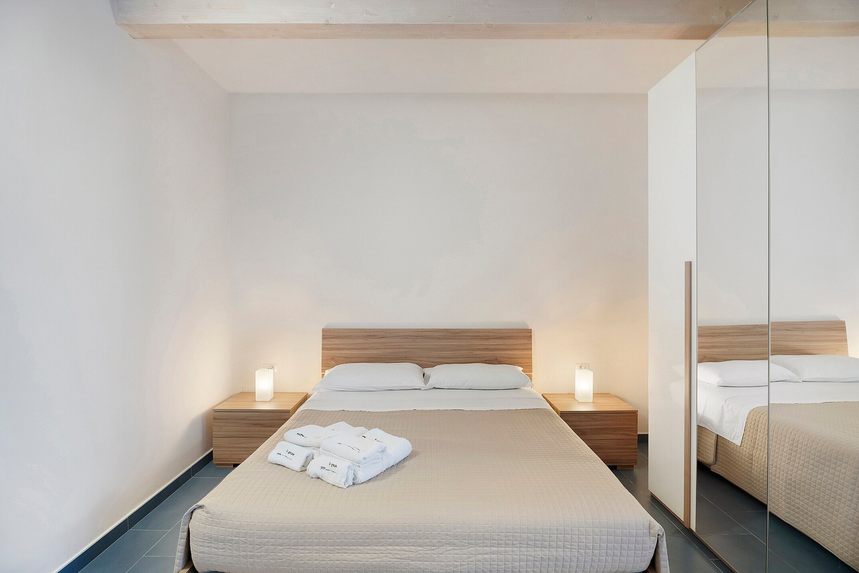 A hotel room with a bed, two bedside tables, a mirror, and a neatly folded towel on the bed.