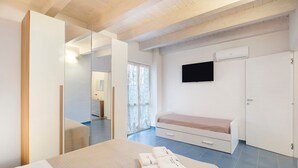Een slaapkamer met een bed, nachtkastje, televisie, kledingkast en een schuifdeur naar een badkamer.