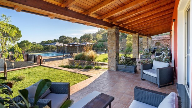 Ein überdachter Patio-Bereich mit Gartenmöbeln, einem Pool und Blick auf die umliegende Landschaft.