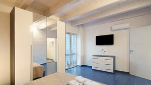 Ein modernes Hotelzimmer mit einem großen Bett, einem Kleiderschrank, einem Fernseher und einem durch eine Glastür einsehbarer Badezimmer.